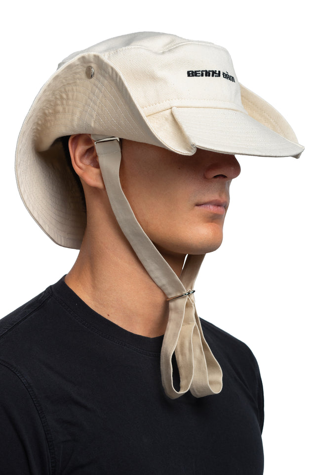 Three quarter front view of floppy bucket hat in bone/eggshell colorway worn on model with side of hat snapped up to show convertibility of style.
