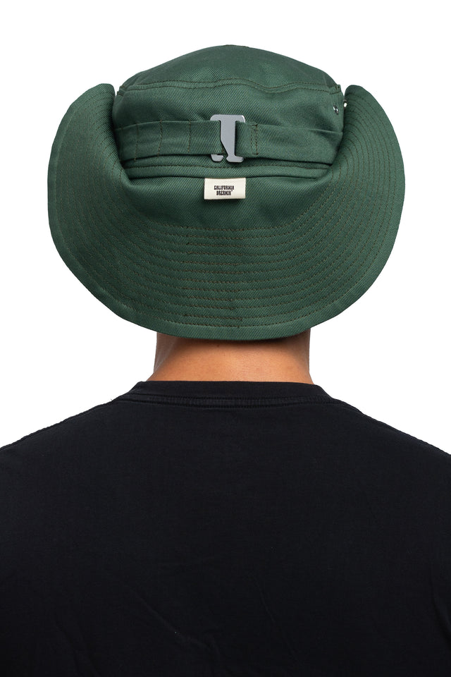 Back view of floppy bucket hat in evergreen/pine colorway worn on model with side of hat snapped up to show convertibility of style.