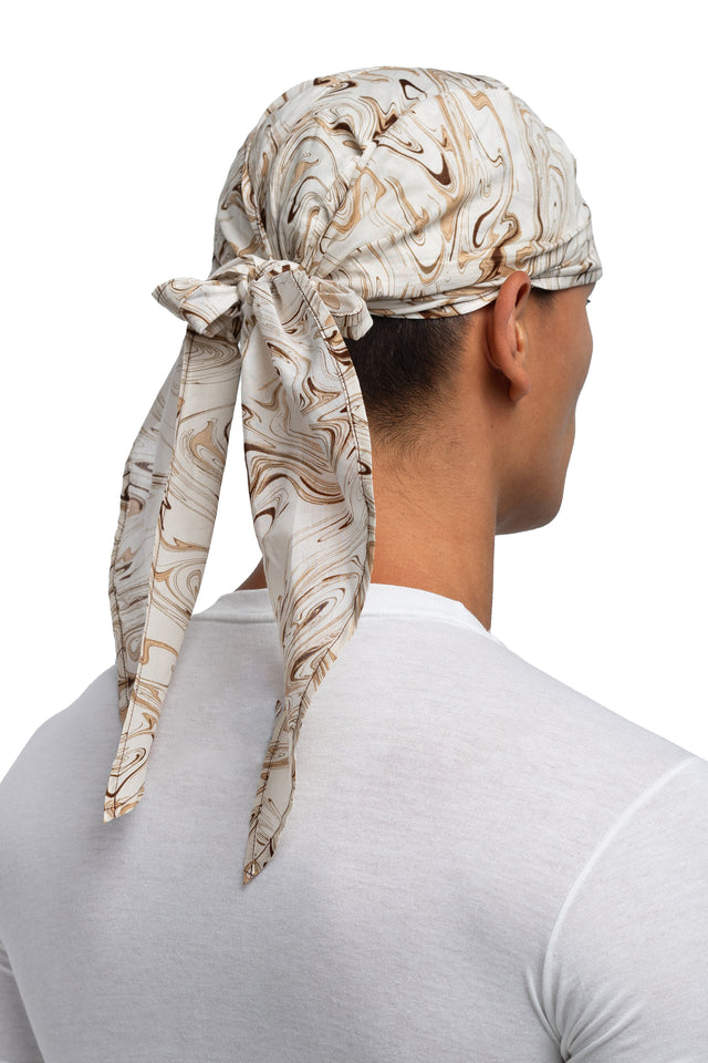 Three quarter back view of brown & cream colorway bandana hat worn on model with side panels tied together.
