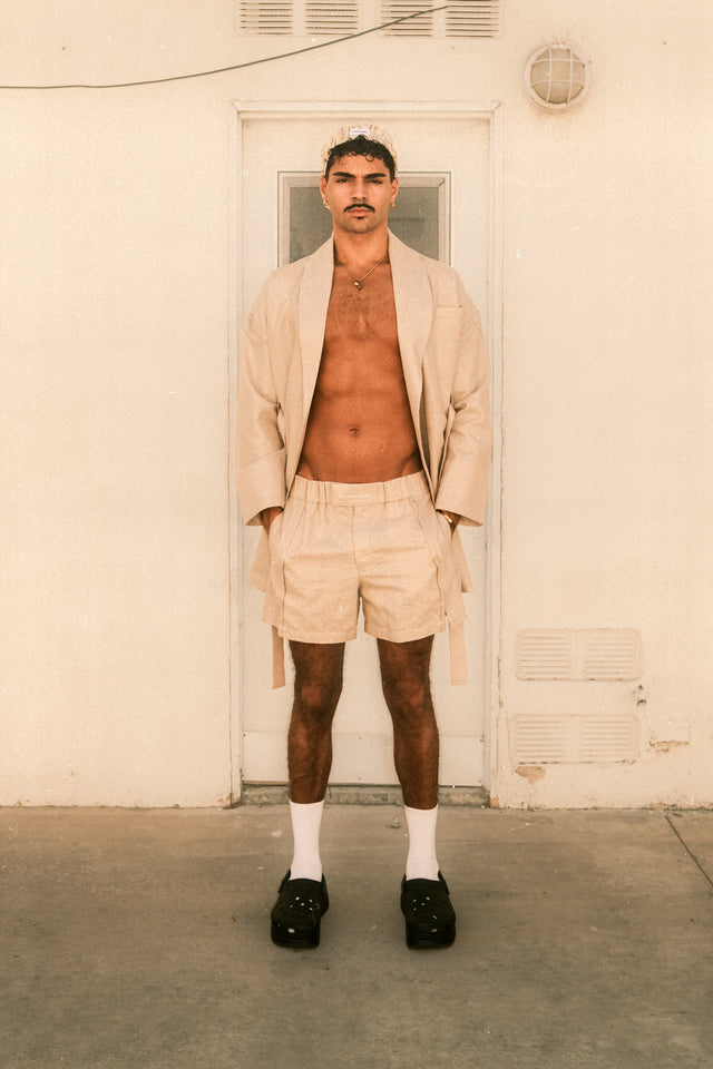 Model wearing metallic gold coat and shorts standing in front of laundry room.